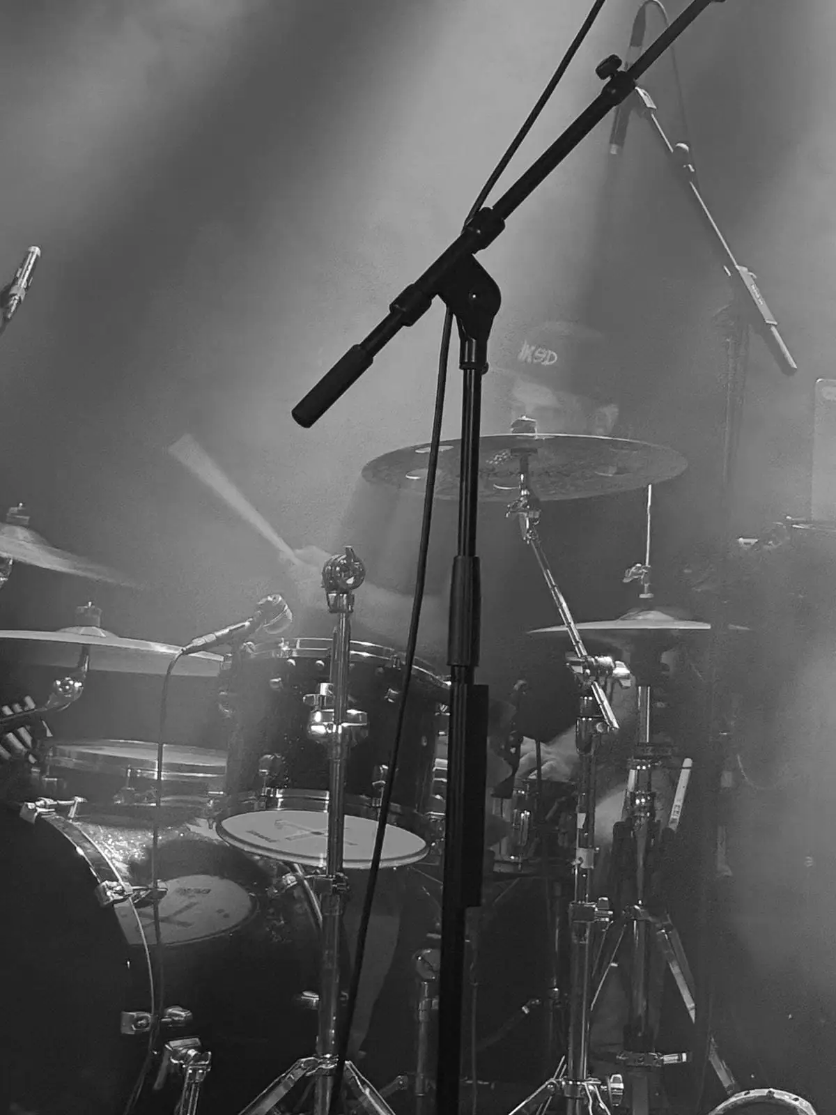 Drummer behind cymbals and microphone stands in thick haze