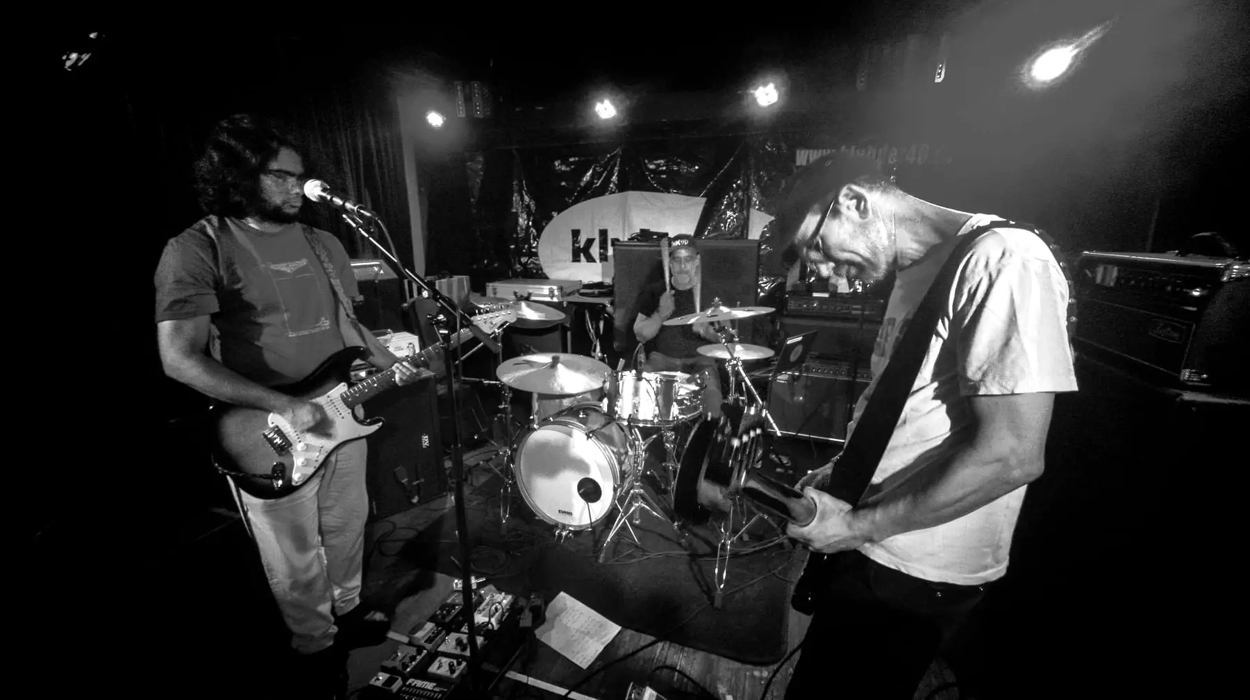 Full stage view: all three band members playing under club lights