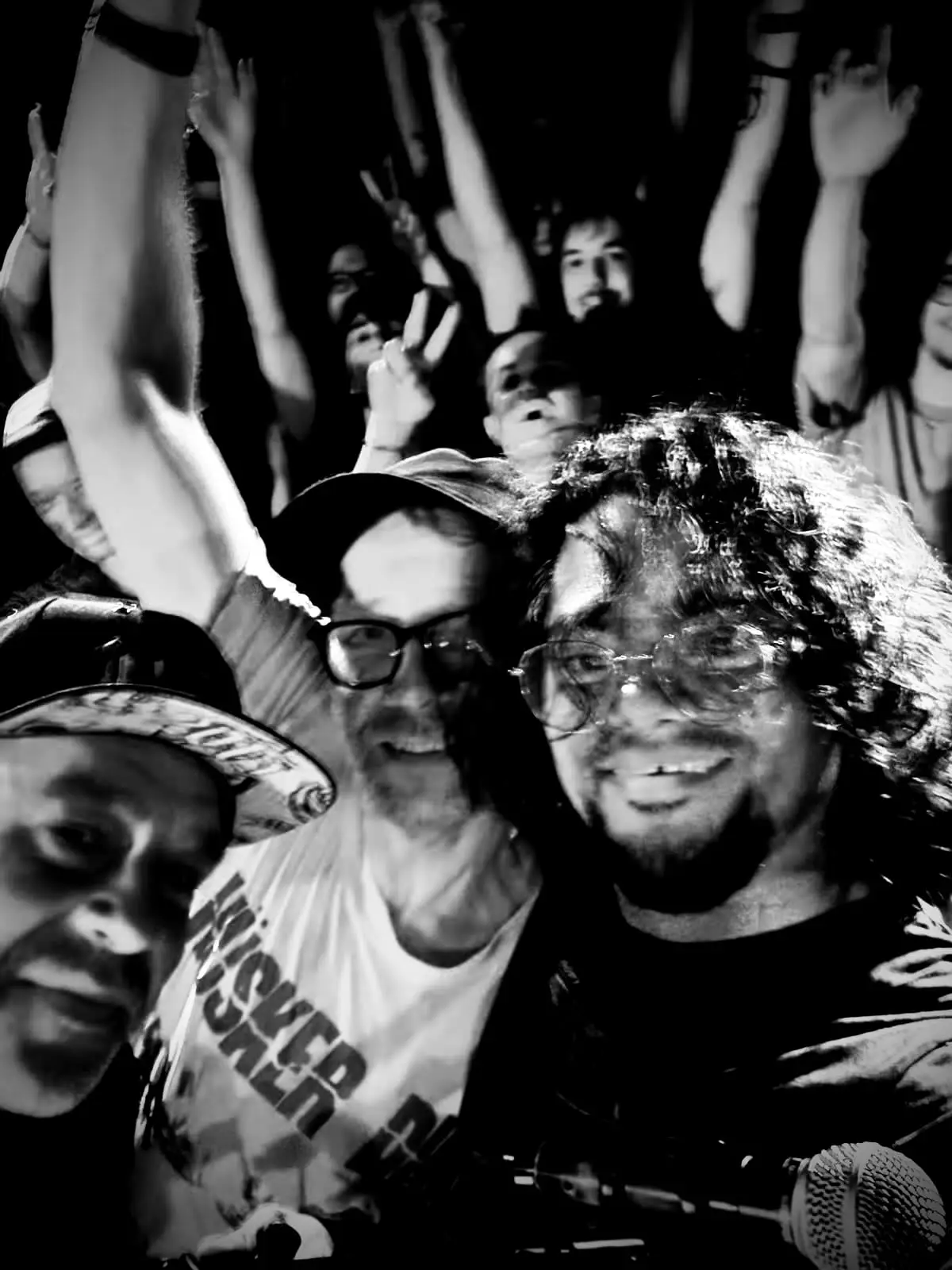 Stage selfie of the band with a cheering crowd behind them