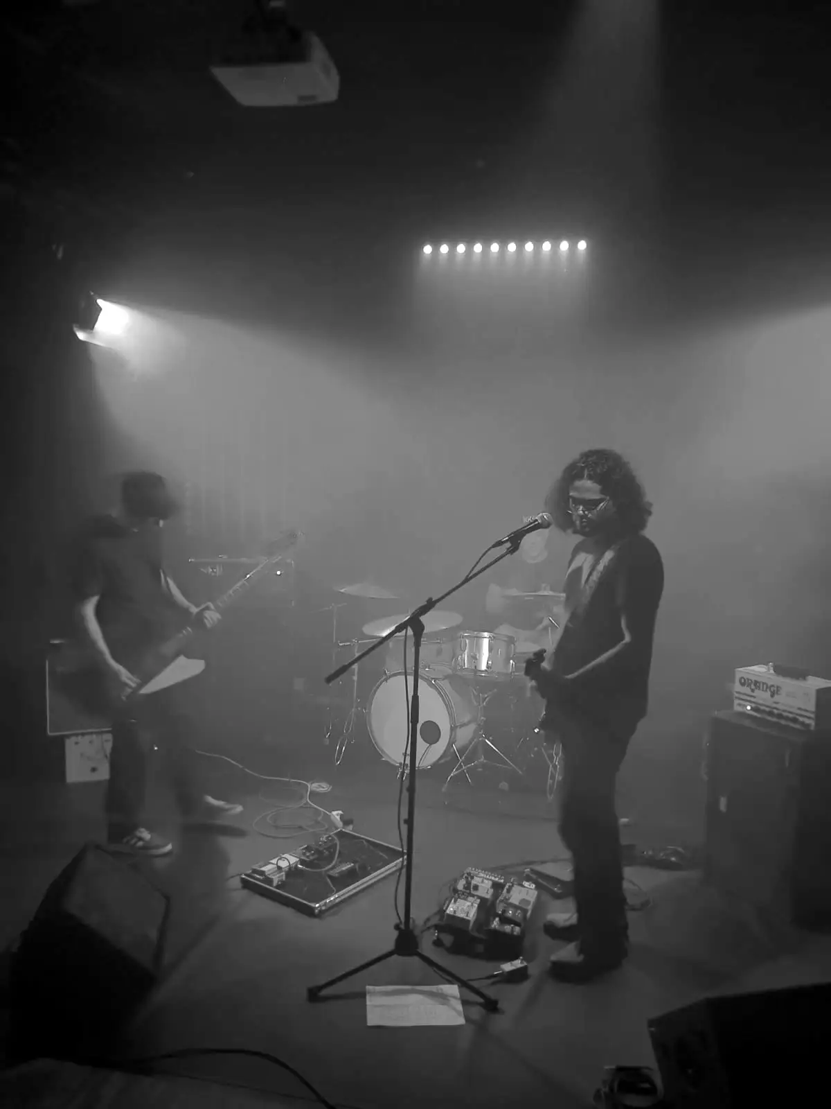 The trio live: guitarist singing at the microphone, bassist on the left, drummer behind